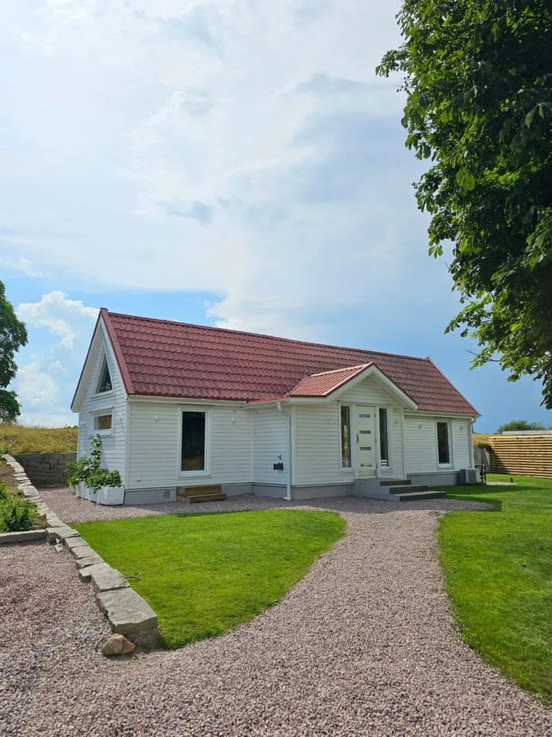 Vitt hus med röda tegeltak och grusuppfart, renoverat